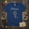 Navy blue t-shirt with white script text "Merci" and a minimalist outline of a hand holding a bouquet of flowers