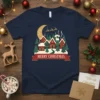 Merry Christmas text on a navy blue t-shirt featuring a snowy village scene with houses, trees, and a crescent moon