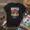 Miami Beach Florida text above a retro sunset with palm trees and a lifeguard stand on a black t-shirt