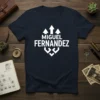 Navy blue t-shirt with white text "MIGUEL FERNANDEZ" and a stylized graphic above and below the name
