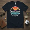 Minnesota Summer North Star State t-shirt design with a circular graphic of pine trees, a lake with canoes, and a