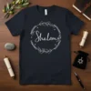Dark t-shirt featuring the text "Shalom" surrounded by a wreath and the phrases "Missing Nothing Hokhing Nothing Lcn Nothing" in