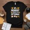 Black t-shirt with the text "MONDAY SHOULD BE OPTIONAL" in bold white font, surrounded by alarm clocks, coffee cups, and