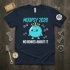 Navy blue t-shirt with "MOOPSY 2028 NO BONES ABOUT IT" text and a cute blue character wearing a crown, surrounded