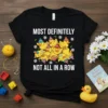 T-shirt with white text "MOST DEFINITELY NOT ALL IN A ROW" above a pile of cute cartoon ducks wearing colorful