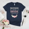 Mother Of The Bride I Loved Her First text with floral graphic on a navy blue t-shirt