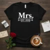 Mrs. EST. 2026 text with arrows on a black t-shirt, representing a future bride's wedding year