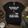 Black t-shirt with white text "MY BLACK LAB ISN'T SPOILED. I'M JUST A WELL TRAINED OWNER" and a graphic of