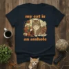 My Cat Is An Asshole humorous quote on a navy t-shirt with a graphic of a mischievous cat near a