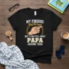 Black t-shirt with white and yellow text: "MY FINGERS May Be Small BUT I CAN STILL WRAP PAPA AROUND THEM"