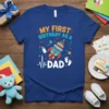 Blue t-shirt with "My First Birthday As A Dad" text and graphics including a rocket cake, baby feet, and heartbeat
