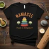 Black t-shirt with "Namaste Peace & Tranquility" text and stacked colorful stones graphic, flanked by lotus flowers