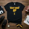Black t-shirt with yellow text "NEXT MAN UP COACH TOMLIN" and chevron graphics, football theme