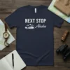 Navy t-shirt with white text "NEXT STOP Alaska" featuring mountains, trees, and a cruise ship graphic
