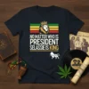 T-shirt with the text "NO MATTER WHO IS PRESIDENT SELASSIE IS KING" in bold white and gold font, featuring a