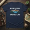 Navy t-shirt with white text "NO ONE IS ILIEGAL ON STOLEN LAND" and mountain and river graphic