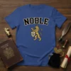 Noble Lion Crest T-Shirt featuring a golden lion holding a shield with a fleur-de-lis, crowned and with the word NOBLE