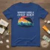 Nobody Likes A Shady Beach quote on a blue t-shirt with a vintage sunset, ocean waves, and beachgoers graphic