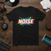 Black t-shirt with the word "NOISE" in bold white lettering, surrounded by a vibrant explosion of red, green, and blue