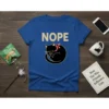 Blue t-shirt with the word "NOPE" in beige text above a sleeping black cat wearing a red and white polka