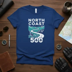 North Coast 500 text and graphic of a winding coastal road with motorcycles and a lighthouse, on a blue t-shirt