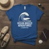 Ocean Breeze Adventures California text with a wave and surfboard graphic on a blue t-shirt
