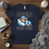Official Sleep Shirt design featuring a cute sleepy highland cow wearing blue striped pajamas and a matching cap, resting on