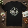 Black t-shirt with "Oh La La" text and Eiffel Tower graphic in a circle, featuring French travel theme