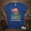 One Nation Under God t-shirt design with American flag, wooden cross, river, mountains, and flowers