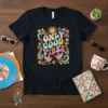 Black t-shirt with "Only Good Vibes" in colorful retro lettering, featuring a smiling sun, birds, and floral accents