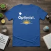 Blue t-shirt with white text "Optimist." and a graphic of a rising sun with a dove flying above