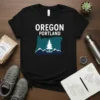 Black t-shirt featuring "Oregon Portland" text above a teal Oregon state outline with a white pine tree and blue mountains