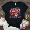 Black t-shirt with "Our Little Sweet Heart Is On The Way" in retro font, featuring baby feet on clouds