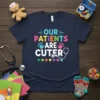Our Patients Are Cuter text design with colorful letters, handprints, and stethoscope graphic on a navy t-shirt