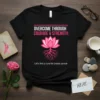 Black t-shirt with "Overcome Through Courage & Strength" and a lotus flower, promoting breast cancer awareness and the search for