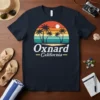 Oxnard California text with retro sunset and palm trees graphic on a dark t-shirt