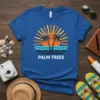 Blue t-shirt with "PALM TREES" text and a retro sunset design featuring palm trees and ocean waves