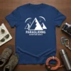 Paragliding Adventure Awaits text on a navy blue t-shirt with graphic of mountains and paragliders