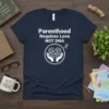 Parenthood Requires Love NOT DNA quote on a navy blue t-shirt with hands holding plants graphic