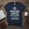 Pastor In It For The Outcome Not The Income quote on a navy t-shirt, with a cross and hands graphic