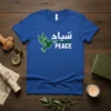 Blue t-shirt with "سلام PEACE" in Arabic and English, featuring a green dove holding an olive branch
