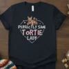 Perfectly Sane Tortie Lady text with a cute tortoiseshell cat illustration inside a heart outline on a black t-shirt