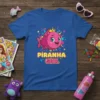 Piranha Girl T-Shirt with a pink cartoon piranha wearing a crown and bow, featuring colorful stars and text