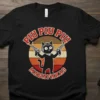 Piu Piu Piu Madafakas text with a black cat holding two guns, retro sunset background, on a black t-shirt