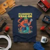 Plumber's Kraken T-Shirt design featuring an orange octopus wearing overalls and a green cap, holding a plunger and wrench amidst