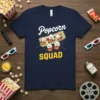 Navy t-shirt with "Popcorn Squad" text and cartoon popcorn characters in superhero capes, with a movie ticket graphic
