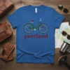 Green bicycle graphic with red text "portland" below, on a blue t-shirt, representing Portland bicycle culture