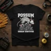 POSSUM URBAN SURVIVOR text with a possum on gears graphic on a black t-shirt