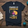 Powered by Crocheting and Cats text design with two cats and a ball of yarn, on a navy t-shirt