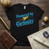 Black t-shirt with "Powered by Curiosity" text and a yellow rocket graphic, designed for science enthusiasts